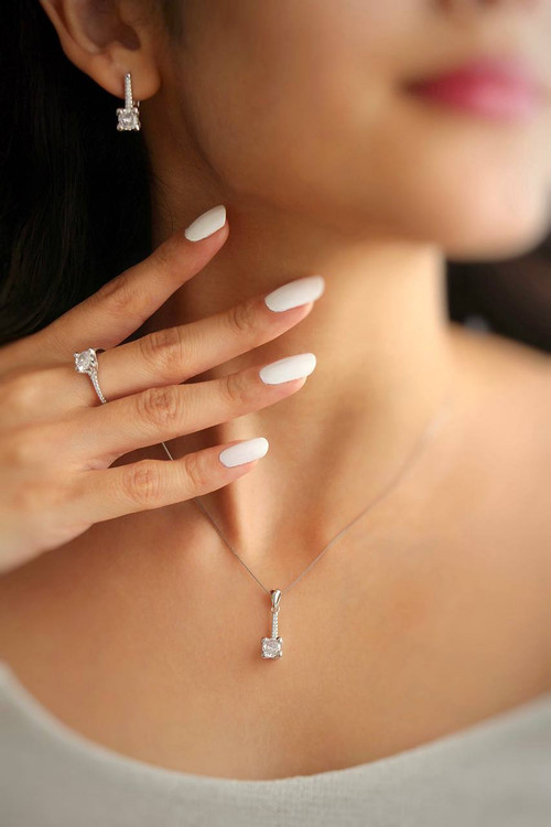 نمای نزدیک از نیمست نقره طرح امرالد روی گردن شامل مدال و گوشواره با تراشهای چهارگوش درخشان.